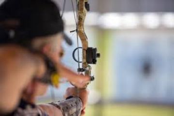 Person aiming a compound bow at a blurred target.